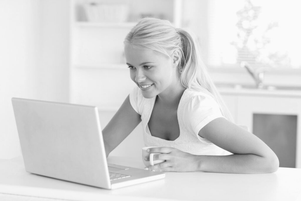 Cute woman having a cup of tea while using her notebook